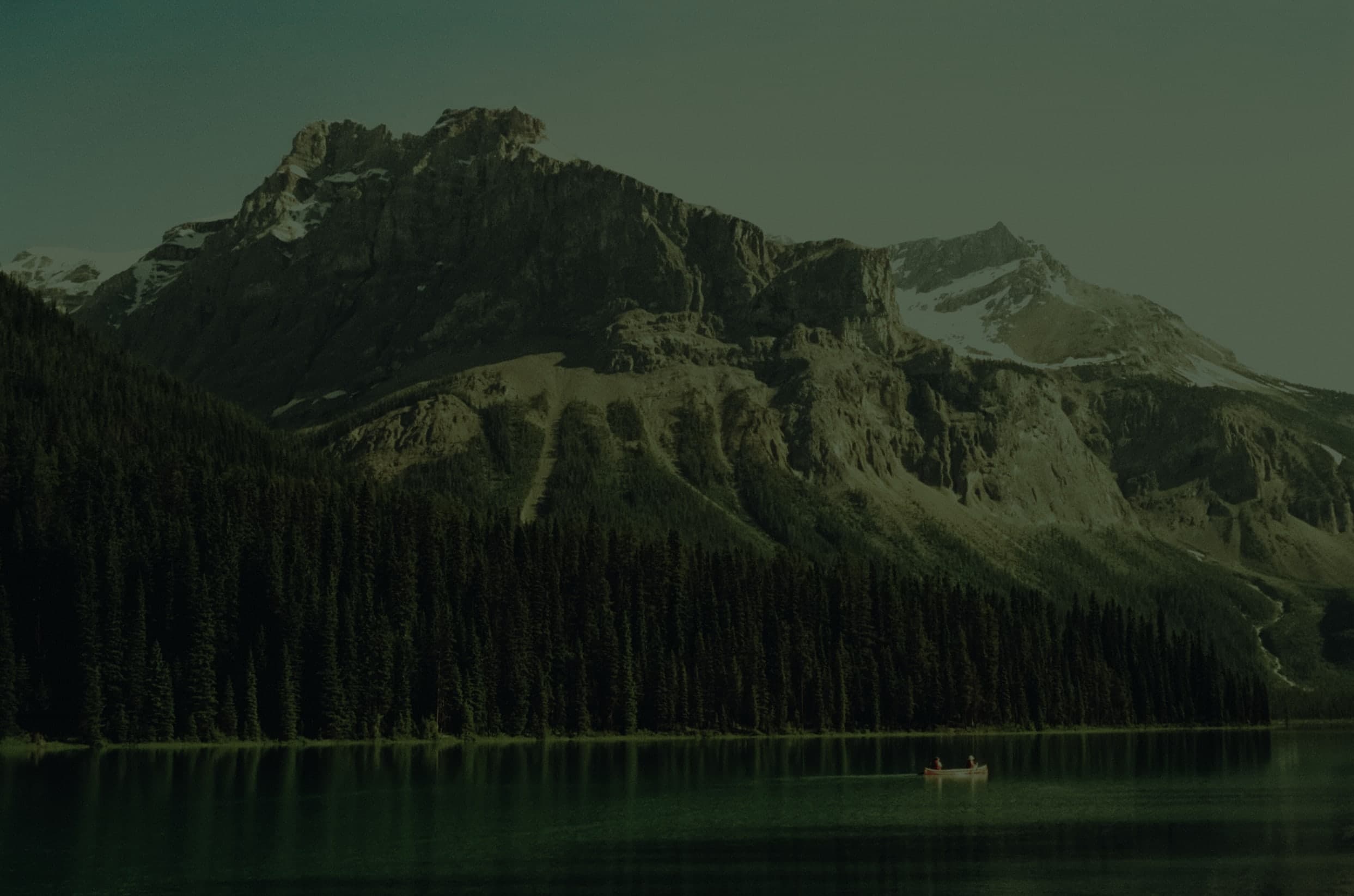 Photo of a lake with trees in the background and two people in a canoe.